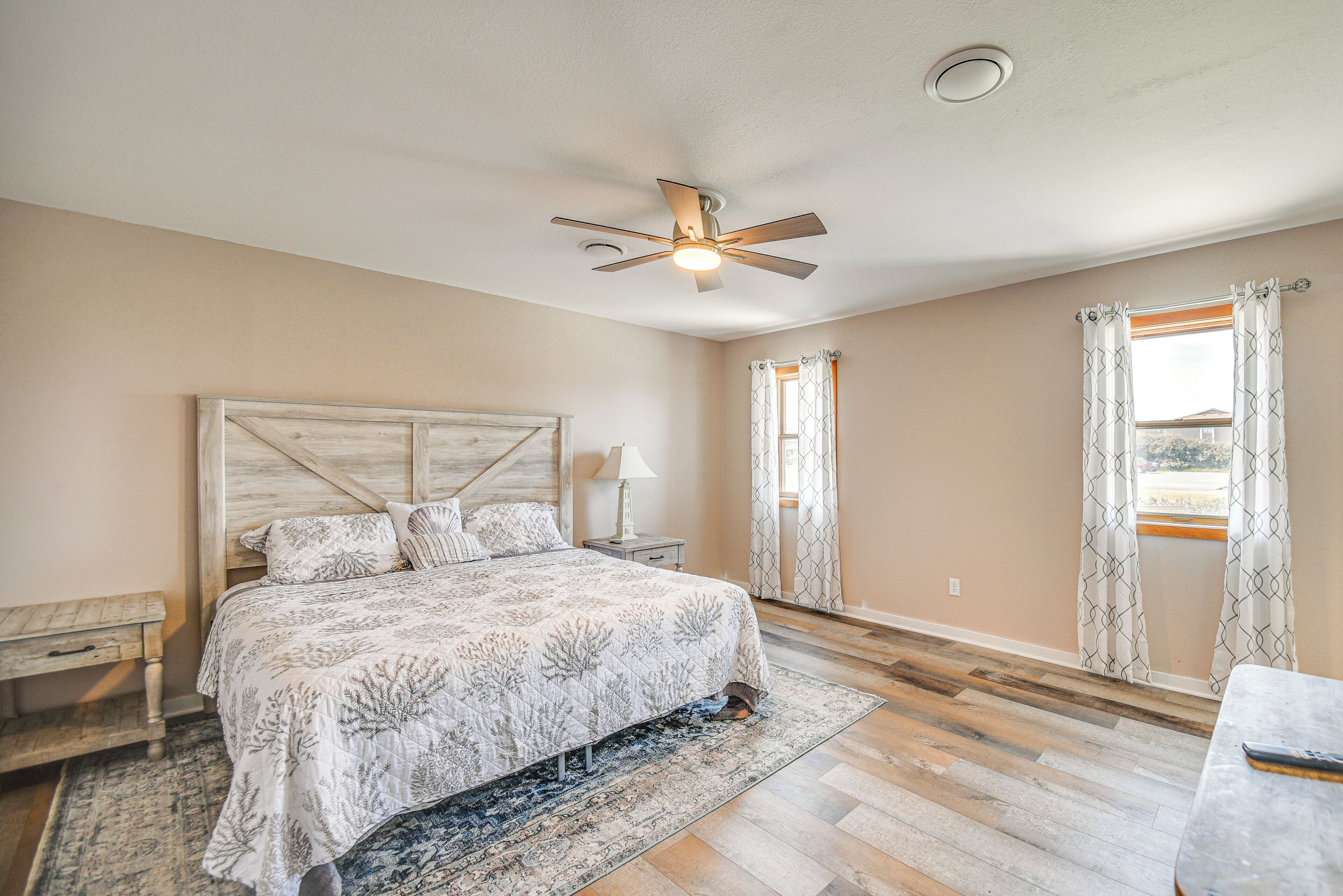 A bedroom with a bed, a nightstand, a ceiling fan, and a window with curtains.