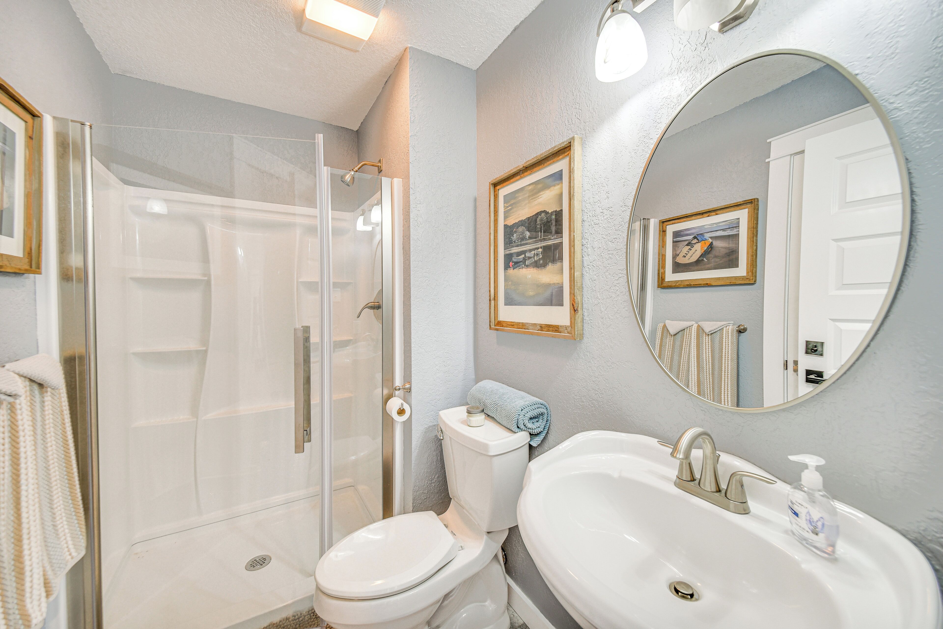 A bathroom with a shower, toilet, sink, and two framed pictures on the wall.