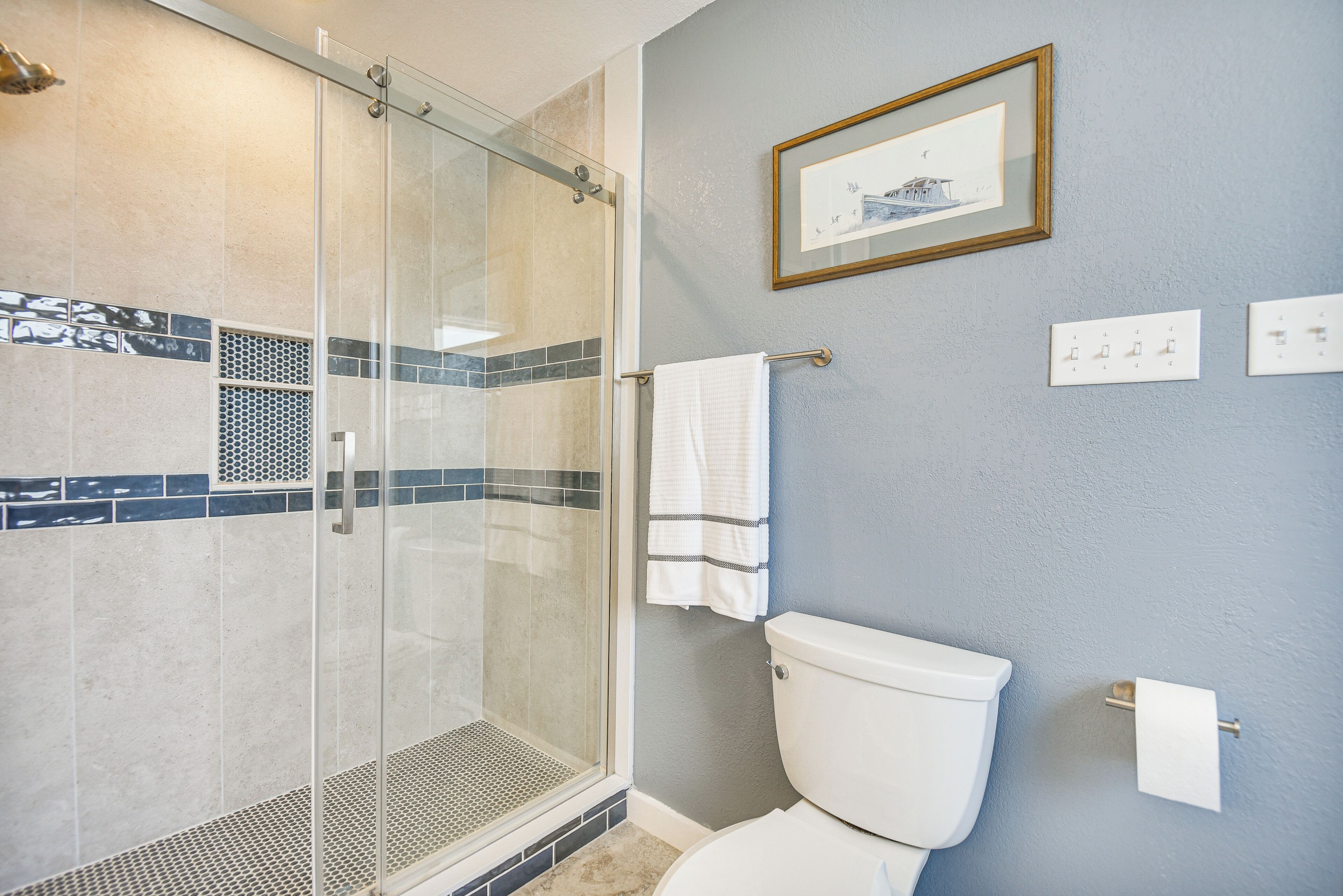 Un baño con cabina de ducha de vidrio, inodoro blanco y un cuadro en la pared.