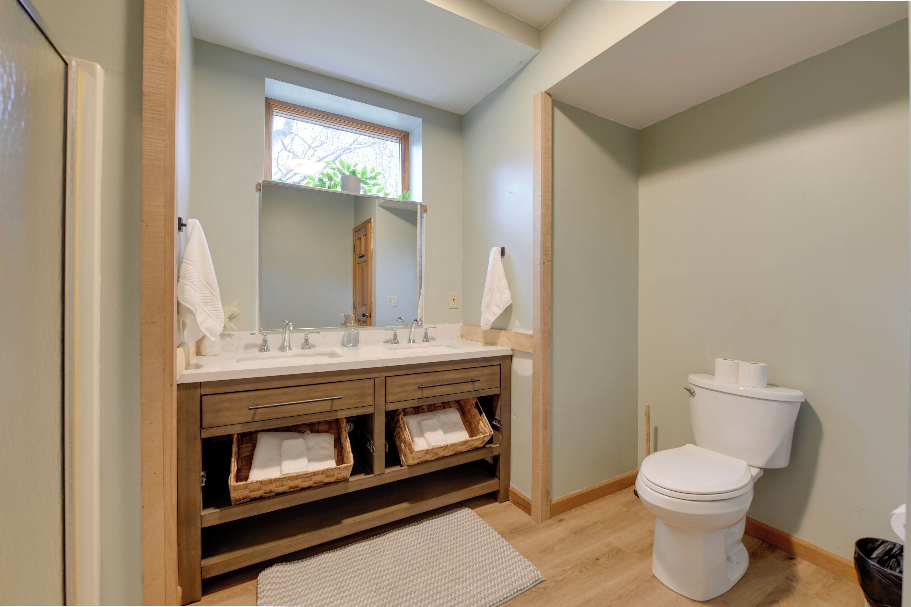A bathroom with a wooden vanity, two sinks, a toilet, and a window.