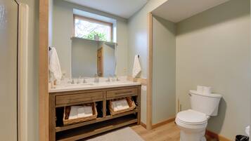 A bathroom with a wooden vanity, two sinks, a toilet, and a window.