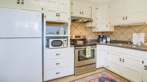Een keuken met witte kasten, een magnetron, een oven, een spoelbak en een betegelde achterwand.