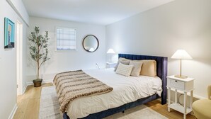 Een slaapkamer met een bed, nachtkastjes, een kamerplant, een spiegel en een raam.