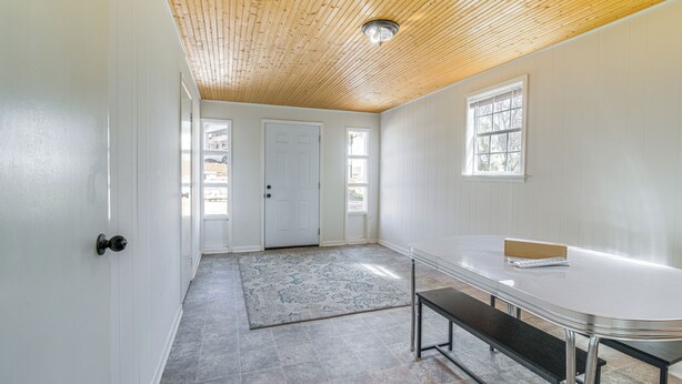 Een ruime kamer met een houten plafond, witte muren, een grote tafel en een bank.