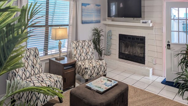 A living room with a fireplace, two patterned armchairs, a coffee table, and a TV mounted above the fireplace.