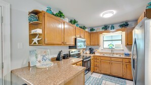A kitchen with wooden cabinets, granite countertops, a stainless steel refrigerator, and a window with blinds.