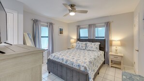A bedroom with a bed, two bedside tables, a ceiling fan, and a window with curtains.