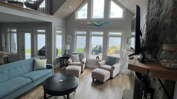 A spacious living room with a high ceiling, large windows, a fireplace, and a view of the outdoors. - Luxury Oceanfront Home in Lunenburg (First South)