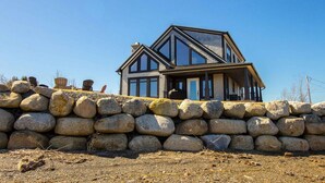 A modern house with a stone wall foundation, large windows, and a prominent gable roof. - Luxury Oceanfront Home in Lunenburg (First South)