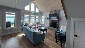 A spacious living room with a large window, a fireplace, and a television. - Luxury Oceanfront Home in Lunenburg (First South)