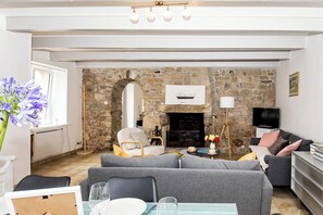 A living room with a stone wall, a fireplace, a television, and a sofa. - Kermané, Maison Chaleureuse Côte des Légendes - Plage à Pieds (Plouescat)