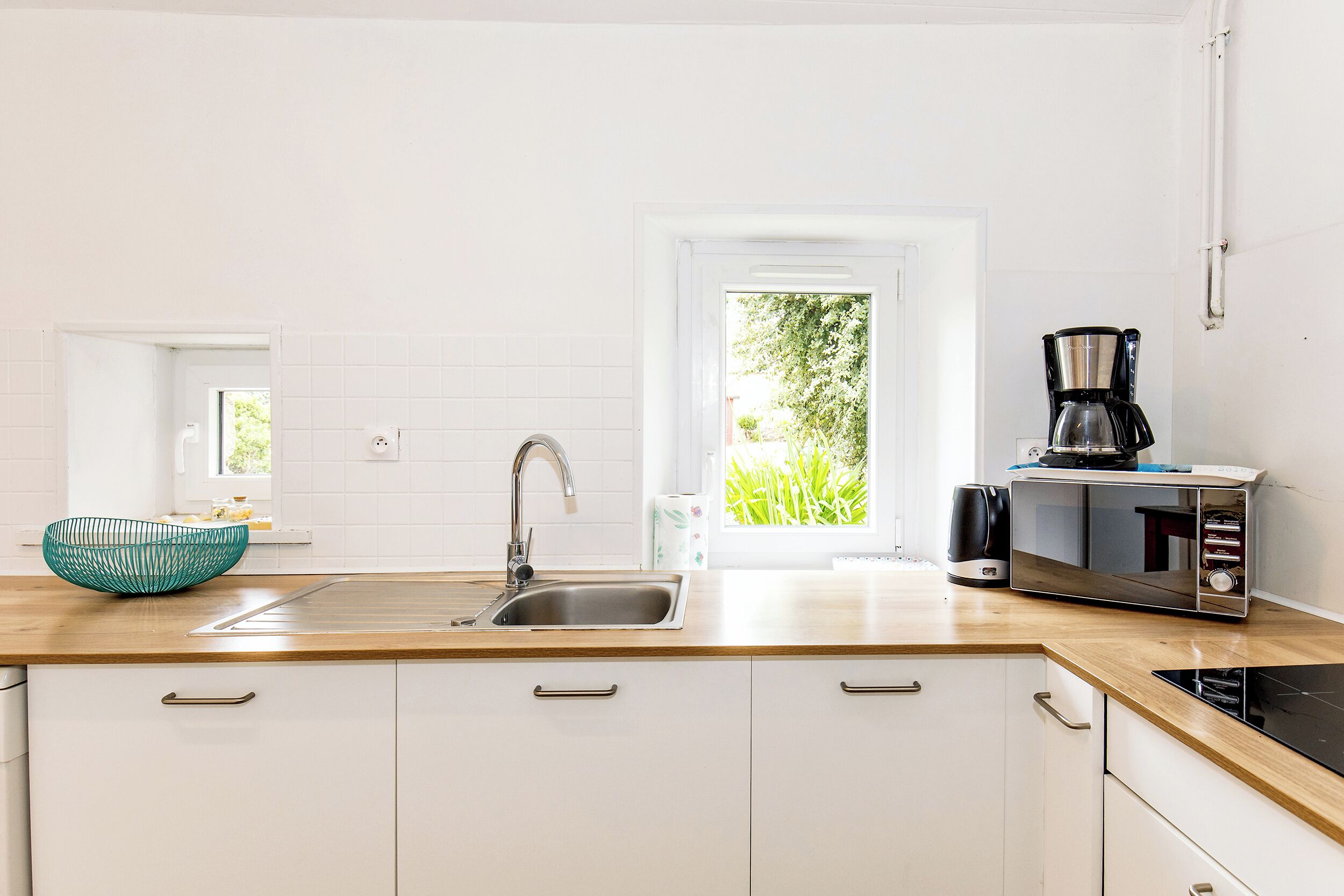 A modern kitchen with a sink, a coffee maker, and a view of greenery outside.