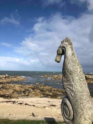 A stone seahorse sculpture on a rocky beach with the ocean in the background.