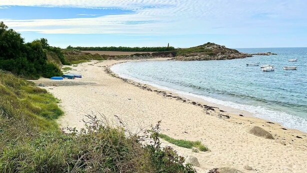 Une plage de sable avec des bateaux, un phare et des affleurements rocheux.