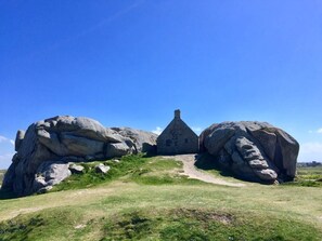 A stone structure with a triangular roof, surrounded by large boulders and a grassy area.