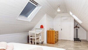 Une chambre avec un plafond en pente, un lit avec des serviettes roulées, un bureau avec une chaise, une armoire et un porte-manteau.