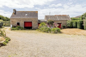 A gravel driveway leading to a stone building with red doors, surrounded by lush greenery and a clear sky. - Kermané, Maison Chaleureuse Côte des Légendes - Plage à Pieds (Plouescat)