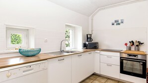 Une cuisine compacte avec des meubles blancs, un lave-vaisselle, une machine à café et un four à micro-ondes.