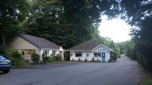 A small building with a reception area, a car parked in front, and a road leading to it. - Immaculate 2-bed Lodge in Nr Mevagissey (St Austell)