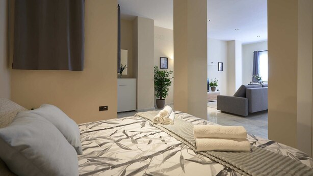 Et moderne soveværelse med en stor seng, en grå sofa og en potteplante.