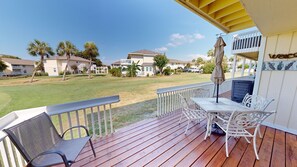Eine Holzterrasse mit Gartenmöbeln, einem überdachten Bereich und Blick auf eine Wohngegend mit Häusern und Palmen.