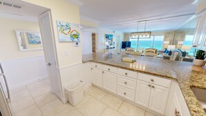 A spacious kitchen with white cabinetry, a granite countertop, and a view of the ocean through large windows. - Beach House 601d 2 Bedroom Condo by RedAwning (Miramar Beach)