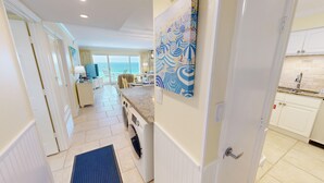 A hotel room with a view of the sea, a kitchen with white cabinets, and a dining area with a table and chairs. - Beach House 601d 2 Bedroom Condo by RedAwning (Miramar Beach)
