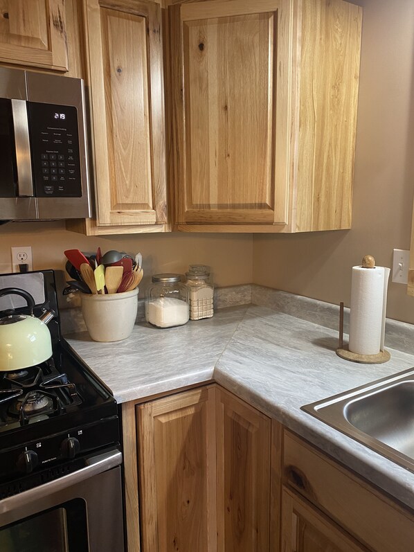 A kitchen with wooden cabinets, a stainless steel microwave, a gas stove, and a marble countertop.