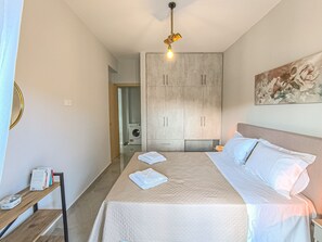 A bedroom with a bed, a wardrobe, a washing machine, and a painting on the wall. - Newly Built House Steps from the Beach: Everything Within Walking Distance! (Agia Marina)