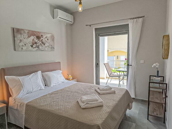 Un dormitorio con cama, mesita de noche, aire acondicionado, ventana con cortinas y vista al exterior.