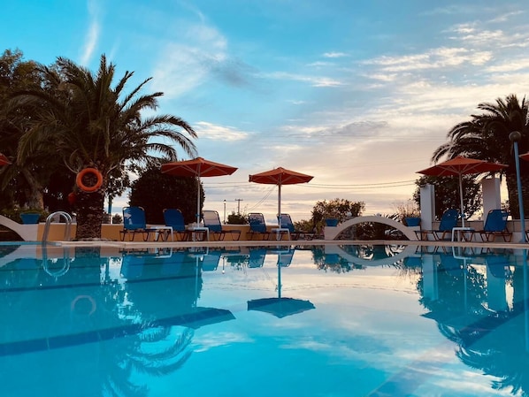 A clear blue pool with lounge chairs and umbrellas, surrounded by palm trees.