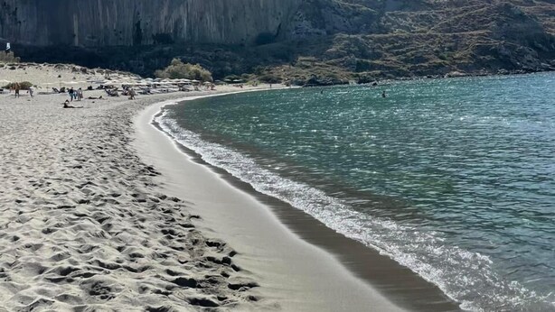 Una playa con aguas cristalinas, una orilla arenosa y una montaña al fondo.