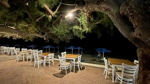 Zona de estar al aire libre con mesas y sillas bajo un árbol grande, con vista a un cuerpo de agua.
