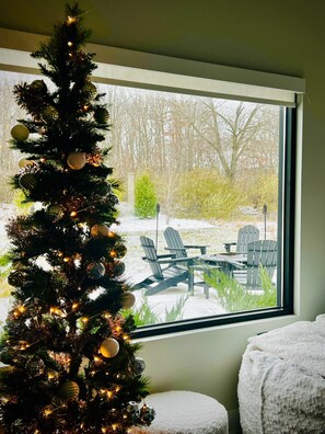 Un sapin de Noël décoré se trouve près d’une fenêtre donnant sur un patio aménagé avec du mobilier d’extérieur.