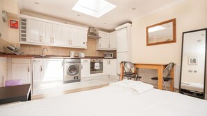 A modern kitchen with white cabinets, a built-in oven, microwave, and washing machine. There is a dining area with a table and chairs, and a large mirror on the wall. - Captivating 1-bed Apartment in London (London)