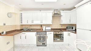 A modern kitchen with white cabinets, a built-in washing machine, a microwave, and a toaster. - Captivating 1-bed Apartment in London (London)