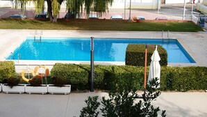 Una piscina rectangular con un deck blanco, rodeada de setos bien cuidados y un paraguas blanco.