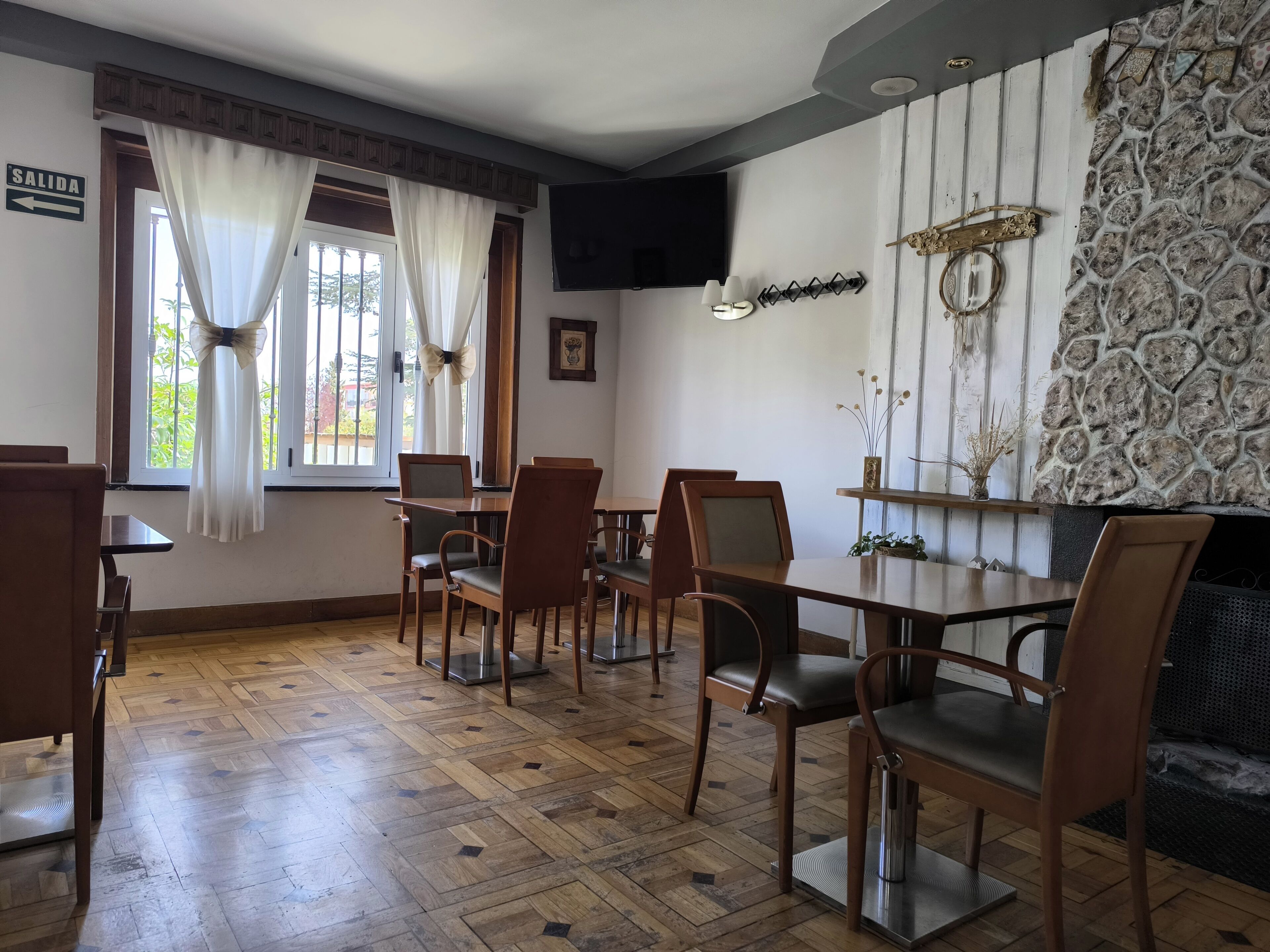 Un comedor con mesas y sillas de madera, una pared de piedra y un televisor instalado en la pared.