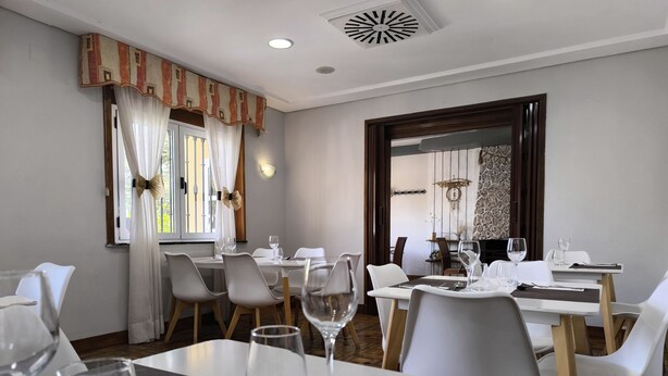 Un comedor con mesas preparadas para dos, cada una con copas de vino y cubiertos.