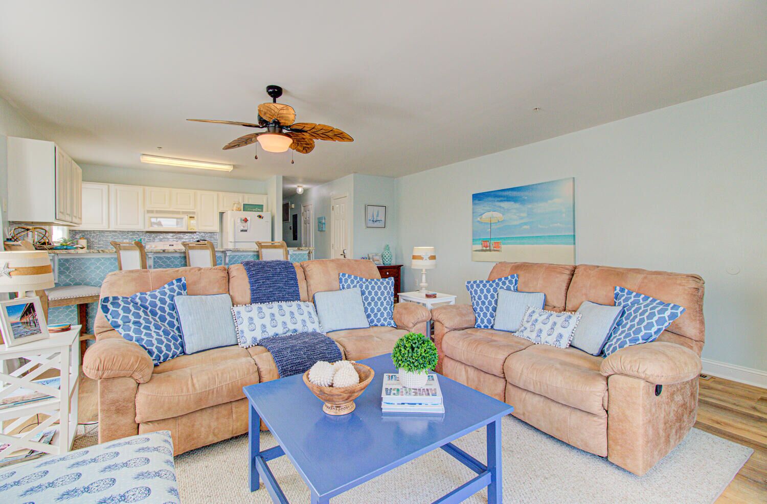 A living room with two beige sofas, a blue coffee table, and a ceiling fan.