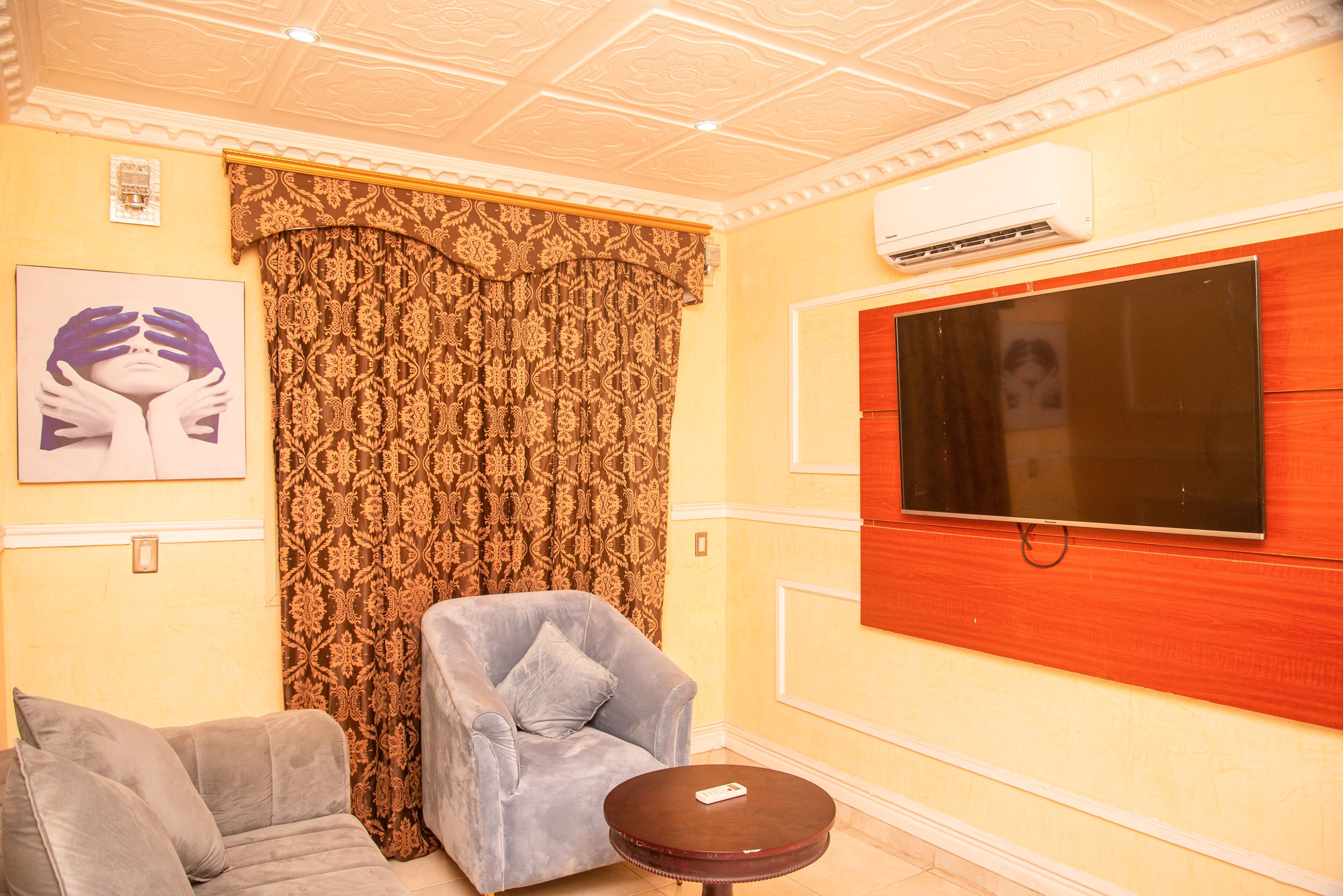 A living room with a sofa, a chair, a small table, a TV, and patterned curtains.