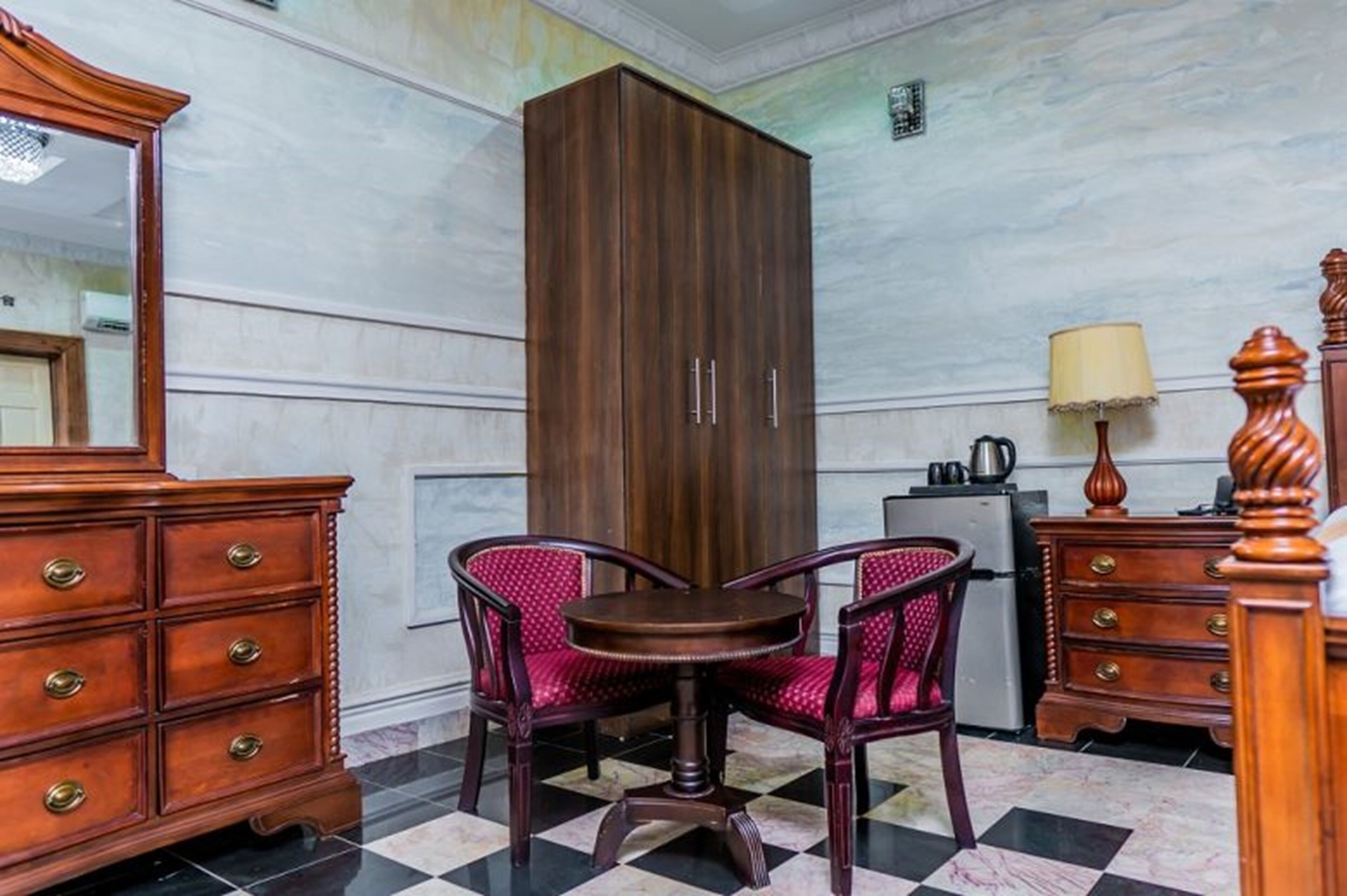 Ein Zimmer mit einem Holzschrank, einem runden Tisch mit zwei Stühlen, einer Kommode und einer Lampe.