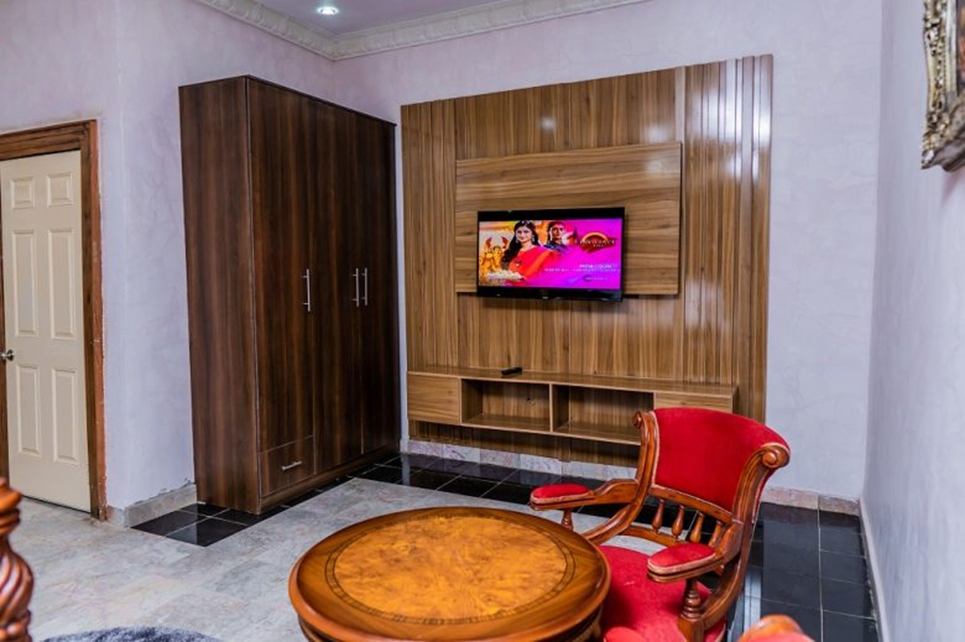 A living room with a TV mounted on a wooden wall, a red chair, and a wooden cabinet.