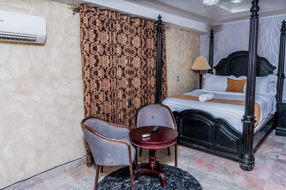 A hotel room with a four-poster bed, a small round table, two chairs, and a patterned curtain.