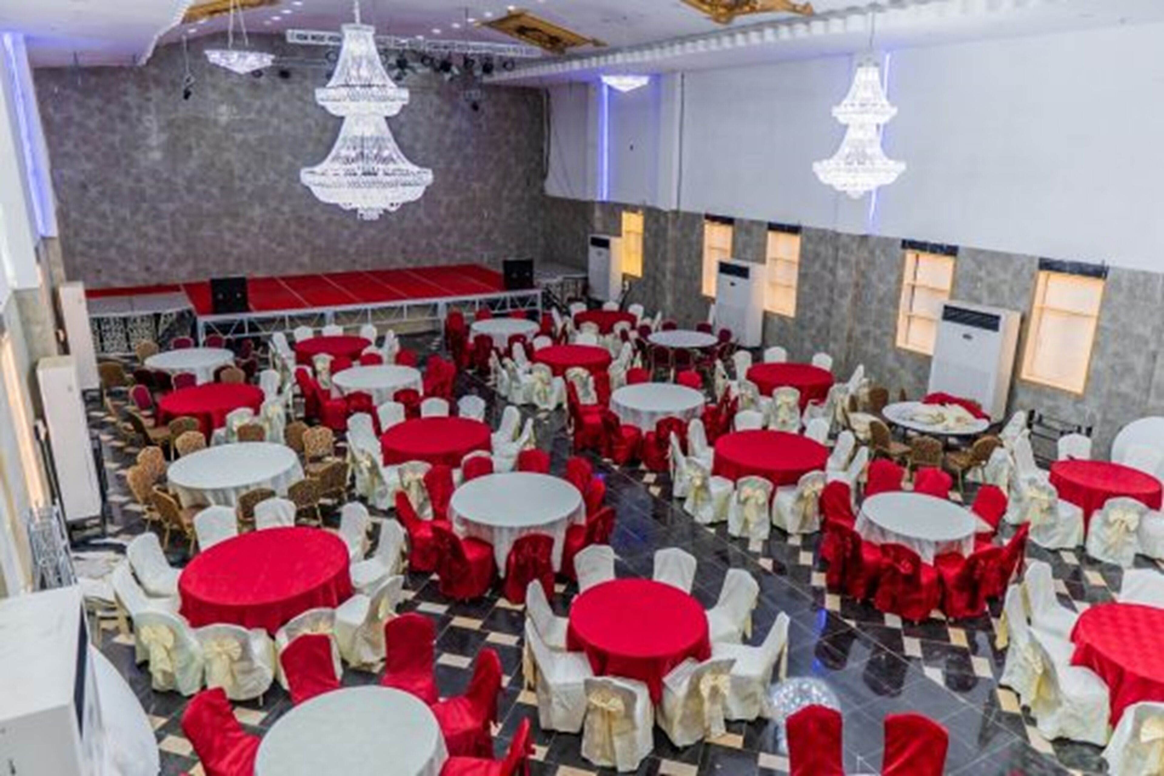 A banquet hall with round tables covered in red tablecloths and white chairs, arranged in a spacious layout.