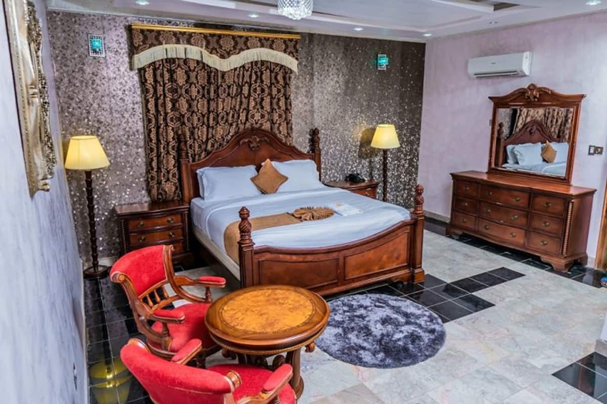 A hotel room with a large bed, a wooden dresser, a red armchair, and a round table.