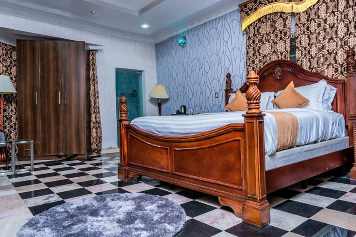 A bedroom with a large bed, a wardrobe, a checkered floor, and patterned wallpaper.