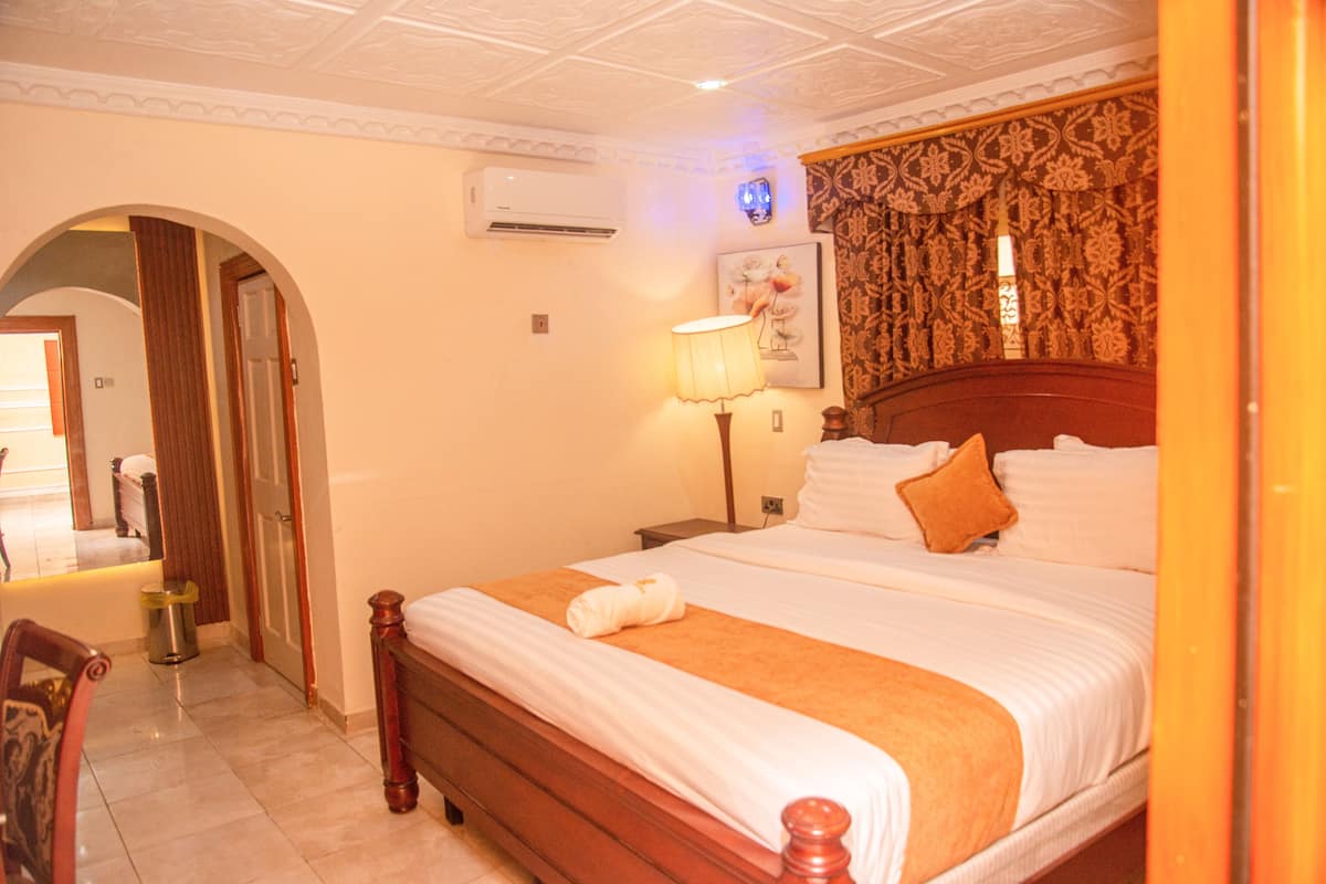 A hotel room with a large bed, a nightstand, a lamp, and a wall-mounted air conditioner.