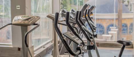 A row of stationary bikes in a gym with a large window in the background.