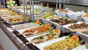 Ein Buffet mit verschiedenen Speisen, darunter Salate, Fleischgerichte und Reisgerichte, präsentiert auf einer Theke mit Servierbesteck.